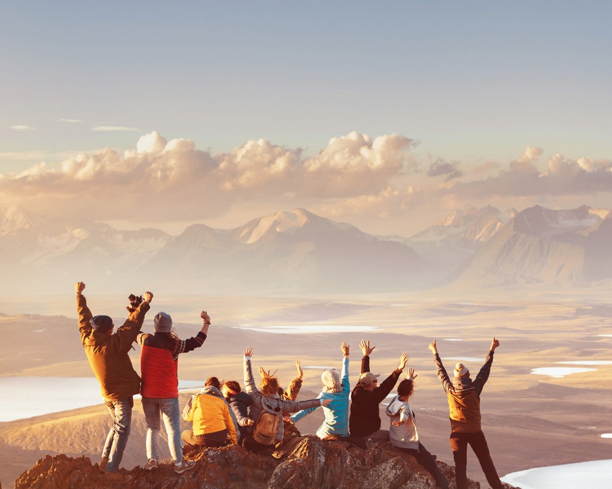 Grupp med lyfta armar på en bergstopp vid solnedgången